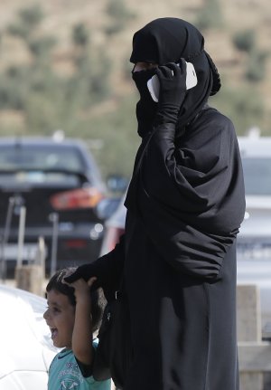 A Syrian refugee uses a mobile phone as she walks with …