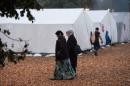 Migrants walk in front of tents in a refugee camp in Celle