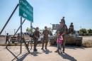 Fighters of the Kurdish People's Protection Units stand with children near a sign in Tel Abyad town