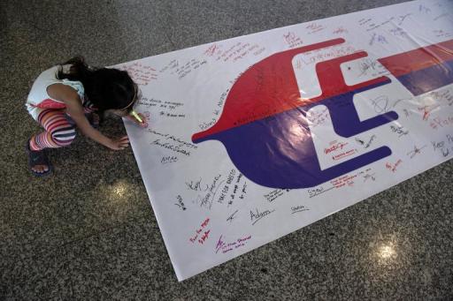 Uma menina escreve em uma faixa com mensagens aos passageiros do avião da Malaysia Airlines, desaparecido há duas semanas, no aeroporto internacional de Kuala Lumpur. Foto de 16 de março de 2014