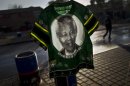 A South African man, right, walks past a T-shirt bearing the image of former South African President Nelson Mandela displayed for sale by a vendor, not pictured, in Soweto township on the outskirts of Johannesburg, South Africa, Monday, July 1, 2013. Former president Nelson Mandela remained in a critical condition at the Medi-Clinic Heart Hospital in Pretoria on Monday . (AP Photo/Muhammed Muheisen)