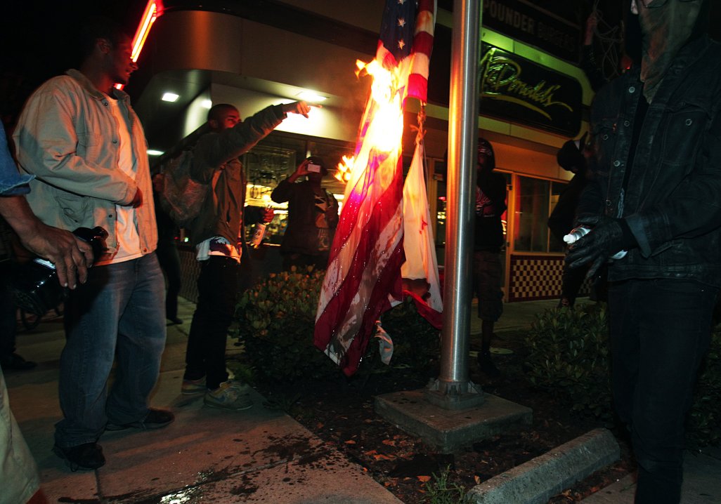 Marchers burn a United States flag outside a fast food restaurant during a protest after George Zimmerman was found not guilty in the 2012 shooting death of teenager Trayvon Martin, early Sunday, July 14, 2013, in Oakland, Calif. Protesters angered by the acquittal Zimmerman held largely peaceful demonstrations in three California cities, but broke windows and started small street fires Oakland, police said. (AP Photo/Bay Area News Group, Anda Chu)