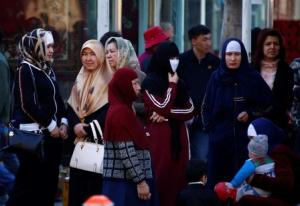 Uighur women stand next to a street   to wait for a bus in downtown Urumqi