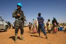 Sudanese people walk past a member of the UN-African Union mission in Darfur at the Zam Zam camp for Internally Displaced People, North Darfur, on April 9, 2015