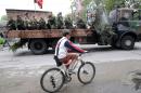 A boy rides a bicycle past combatants onboard a truck attending the memorial service and the funeral of Aleksey Mozgovoi, a militant leader of the separatist self-proclaimed Luhansk People's Republic, and his subordinates in Alchevsk