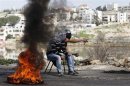 Palestinians sit next to a burning tyre during clashes with Israeli troops near Ramallah