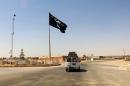 This Tuesday, July 22, 2014 photo shows a motorist passing by a flag of the Islamic State group in central Rawah, 175 miles (281 kilometers) northwest of Baghdad, Iraq, nearly six weeks since a Sunni militant blitz led by the Islamic State extremist group seized large swaths of northern and western Iraq. (AP Photo)