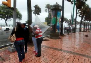 People stand in the rain on a sidewalk of the malecon &hellip;