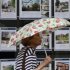 A woman holds an umbrella as she walks past the window of an estate agents office in Manchester
