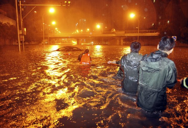 Rescuers use a rope to pull out a stranded car amid heavy rainfall on a flooded street under the Guangqumen overpass in central Beijing