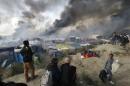 Smoke rises the sky as migrants and journalists look at burning makeshift shelters and tents in the "Jungle" on the third day of their evacuation as part of the dismantlement of the camp called the "Jungle" in Calais