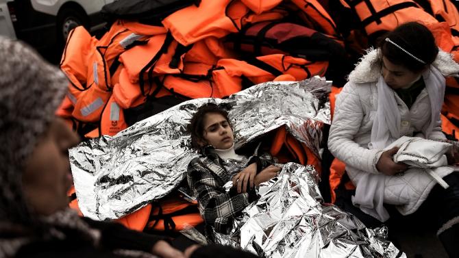 A girl wrapped in a survival blanket lies on life jackets as migrants and refugees arrive on the Greek island of Lesbos while crossing the Aegean Sea from Turkey on March 2, 2016