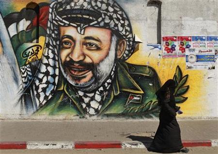 A Palestinian woman walks past a mural depicting late leader Yasser Arafat (R) in Gaza City July 4, 2012. The Palestinian Authority agreed on Wednesday to the exhumation of Arafat's body after new allegations that he was poisoned with the radioactive element polonium-210 in 2004. REUTERS/Mohammed Salem