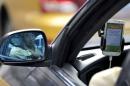 A taxi driver is reflected on a side mirror as he uses Didi Chuxing car-hailing application in Beijing