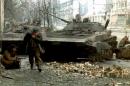 A Chechen fighter runs for cover as another hides behind a destroyed Russian tank during fighting in Grozny, Russia, January 8, 1994