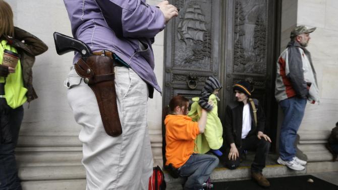 A woman stands with a pistol strapped to her hip as parents, also armed, of a toddler sit behind during a rally by gun-rights advocates Saturday, Feb. 7, 2015, in Olympia, Wash. Approximately 50 demonstrators, including a half-dozen small children, protested rules that prohibit openly carrying guns into the House and Senate viewing galleries. (AP Photo/Elaine Thompson)