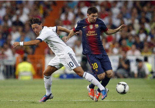 Real Madrid's Mesut Ozil is challenged by Barcelona's Lionel Messi during their Spanish Super Cup second leg soccer match at Santiago Bernabeu stadium in Madrid