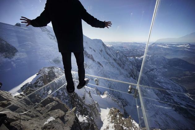 A journalist, wearing slippers to protect the glass floor, stands in the &#39;Step into the Void&#39; installation during a press visit at the Aiguille du Midi mountain peak above Chamonix, in the Fre