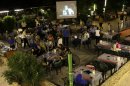 In this picture taken on Wednesday July 24, 2013, Lebanese and Syrian citizens gather at an outdoor coffee shop, as one of the Syrian popular series Al-Wiladah Men Al-Khasira (Birth from the Waist), is broadcast on a giant screen, in Beirut, Lebanon. Birth from the Waist is one of several Syrian soap operas airing during the Muslim holy month of Ramadan this year, almost all of them dealing with the Syrian civil war, now in its third year, spotlighting a conflict in which more than 100,000 people have been killed and millions of others uprooted from their homes. The series have captivated millions of viewers across the Arab world. (AP Photo/Hussein Malla)