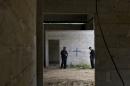 FILE - In this July 3, 2014, file photo, state police stand inside a warehouse where a black cross covers a wall near blood stains on the ground, after a shootout between Mexican soldiers and alleged criminals on the outskirts of the village of San Pedro Limon, in Mexico state, Mexico. Officials said Sunday Nov. 1, 2014, that seven Mexican soldiers have been charged with crimes ranging from homicide to improper conduct in connection with the shooting deaths of suspected gang members at a rural warehouse on June 30. (AP Photo/Rebecca Blackwell, File)