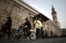 Syrians ride their bicycles past the Omeyyad mosque in Damascus on January 17, 2014