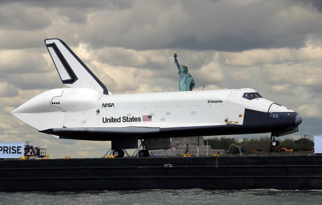 The Space Shuttle Enterprise, passes the Statue of Liberty as it rides on a barge in New York harbor