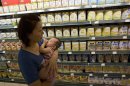 A woman carries a child past powdered milk products including cans of Dumex infant formula already inspected and deemed to be from a safe batch at a supermarket in Beijing, Monday, Aug. 5, 2013. The official Xinhua News Agency said Hangzhou Wahaha Health Food Co. Ltd., Hangzhou Wahaha Import & Export Co. Ltd., Shanghai Tangjiu (Group) Co. Ltd. and Shanghai-based Dumex Baby Food Co. Ltd. on Sunday began recalling and sealing products with allegedly contaminated whey protein from New Zealand. (AP Photo/Ng Han Guan)
