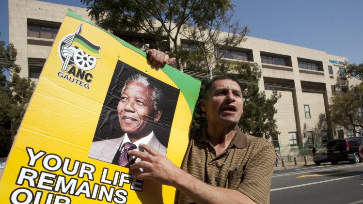 A man only known as Kobus, holds a ruling party poster with former South African President Nelson Mandela's face outside the Mediclinic Heart Hospital where he is being treated in Pretoria, South Africa Wednesday, July 17, 2013. (AP Photo/Themba Hadebe)