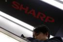 Shopper using a smartphone rides an escalator past under a logo of Sharp Corp at an electronics shop in Tokyo