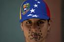 A woman wearing a cap representing Venezuela's national flag, the SOS distress signal marked across her lips and painted black tears streaming down her face, looks into the camera during a demonstration in Caracas, Venezuela, Saturday, March 8, 2014. Venezuelans returned to the streets for the "empty pots march" to highlight growing frustration with shortages of some everyday items. In Caracas, the march was scheduled to end at the country's Food Ministry, but the evening before Caracas' mayor announced that he had not authorized the march. (AP Photo/Fernando Llano)