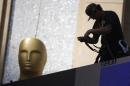 A worker hangs lights next to an Oscar statue outside the Dolby Theatre in preparation for the 87th Academy Awards in Hollywood
