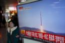 A passenger walks past a TV screen broadcasting a news report on North Korea's long range rocket launch at a railway station in Seoul