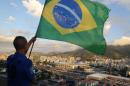 A youth waves a Brazilian national flag on a rooftop in the Mangueira slum, backdropped by Maracana Stadium, in Rio de Janeiro, Brazil, Thursday, June 12, 2014, as he waits for the broadcast of the World Cup opening match between Brazil and Croatia. Brazil won Croatia 3-1. (AP Photo/Leo Correa)