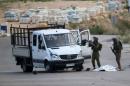 The body of a Palestinian lies covered on the ground as Israeli soldiers inspect the scene near Beituniya