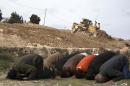 Palestinian protestors pray as a bulldozer hired by the Israeli municipality clears the land for a new national park to be built in annexed East Jerusalem's al-Tur neighborhood, on February 6, 2012