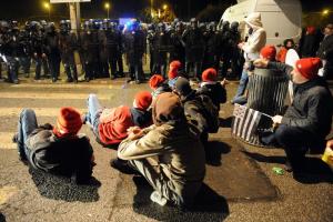 Riot police stand guard as protesters sit during a …