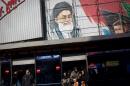 Iranians wait at a bus station under a mural of Iran's supreme leader, Ayatollah Ali Khamenei, at Enghelab (Revolution) square in Tehran