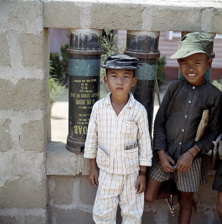 Hai cậu bé đứng trước một bức tường làm từ vỏ bình đựng xăng dầu.