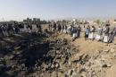People gather around a crater cause by an air strike in Amran province