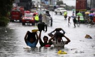 Un grupo de personas trata de no mojar sus pertenencias al cruzar una calle completamente inundada en Filipinas tras el paso del mismo tifón que azotó el sureste de China. EFE/Archivo