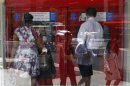 Pedestrians are reflected in the window as customers conduct transactions at a Bank of America ATM in Washington