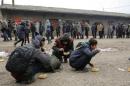 Migrants eat as others stand in line to receive free food outside a derelict customs warehouse in Belgrade