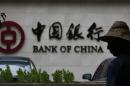 A man is silhouetted in front of a Bank of China's logo at its branch office in Beijing