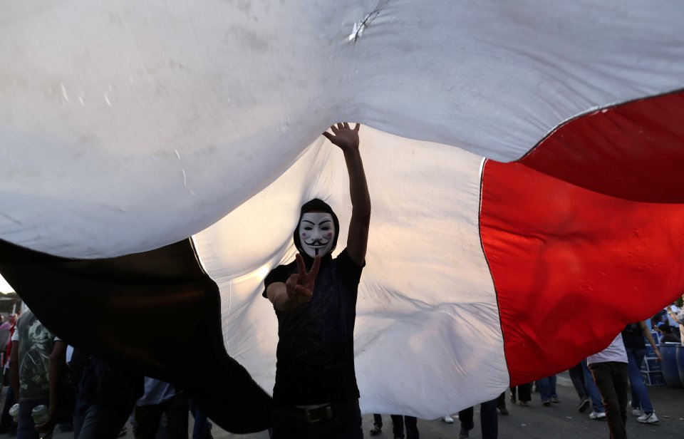 An opponent of Egypt's Islamist President Mohammed Morsi wearing a Guy Fawkes mask flashes the victory sign under a large Egyptian national flag during a protest outside the presidential palace, in Cairo, Egypt, Tuesday, July 2, 2013. Egypt was on edge Tuesday following a "last-chance" ultimatum the military issued to Mohammed Morsi, giving the president and the opposition 48 hours to resolve the crisis in the country or have the army step in with its own plan. (AP Photo/Hassan Ammar)