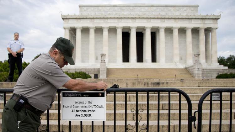 FILE - This Oct. 1, 2013 file photo shows a US Park Police officer watching at left as a National Park Service employee posts a sign on a barricade closing access to the Lincoln Memorial in Washington. About half of Americans expect 2014 to be a better year than 2013, according to the recent AP-Times Square New Year’s Eve poll, and judging by the standard questions pollsters use to measure the public mood, it doesn’t seem like it could be much worse. (AP Photo/Carolyn Kaster, File)