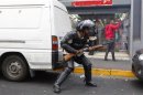Riot police officer takes cover behind a car as he attempts to break up a demonstration in Caracas