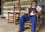 In this Friday, Aug. 10, 2012 photo, James Davis holds a photo of his late wife, Patsy Davis, on the porch of their home in Stevenson, Ala. Davis buried his wife in their front yard, and the city filed suit to force him to remove the remains. Davis is fighting a court order requiring him to disinter the body. (AP Photo/Jay Reeves)