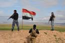 Iraqi government forces stand next to a national flag as they secure an area in Al-Fatha north of the Salaheddin province on January 9, 2015