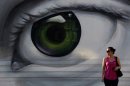A woman waits to cross the road in front of a mural of an eye in Athens, on Friday, Sept. 6, 2013. (AP Photo/Petros Giannakouris)