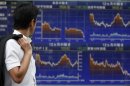 A man looks at an electronic board displaying graphs of various market indices outside a brokerage in Tokyo